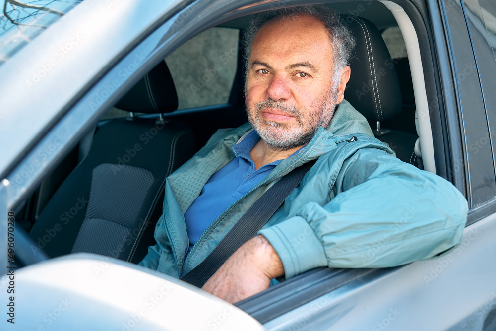 Happy smiling bearded mature man looking out the car window sitting behind the wheel of a prestigious car. Happy smiling bearded mature man looking out the car window sitting behind the wheel of a prestigious car.