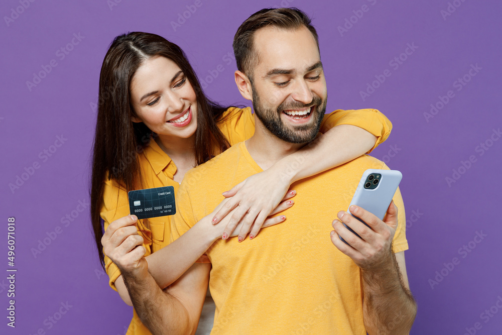 Young couple two friends family man woman together in yellow clothes using mobile cell phone hold credit bank card do online shopping order delivery booking tour isolated on plain violet background