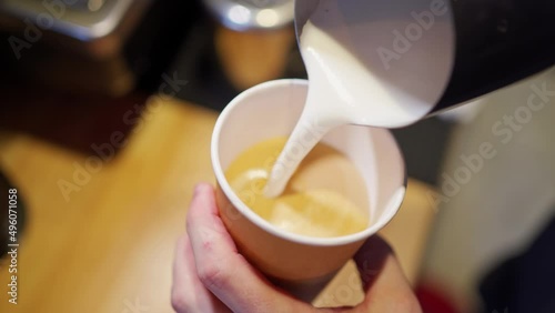 barista hands making latte art pouring frothed milk from a pitcher into a disposable paper cup with espresso coffee