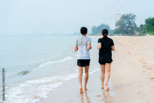 A young Asian couple, jogging comfortably by the sea, and the cool sea waves crashing against their feet, a popular tourist destination.