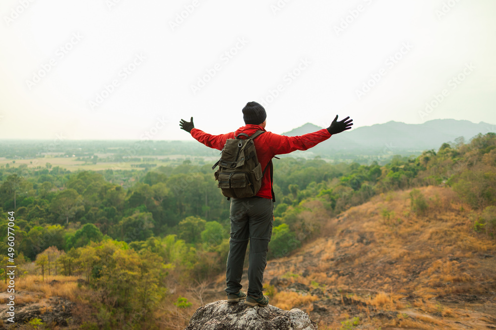 Asian young man conquers the peak success in life goals. Young asian man mountaineering wearing jacket walking at outdoor. Hiker with backpack and trekking pole. Asian young man conquers the peak success in life goals. Young asian man mountaineering wearing jacket walking at outdoor. Hiker with backpack and trekking pole.