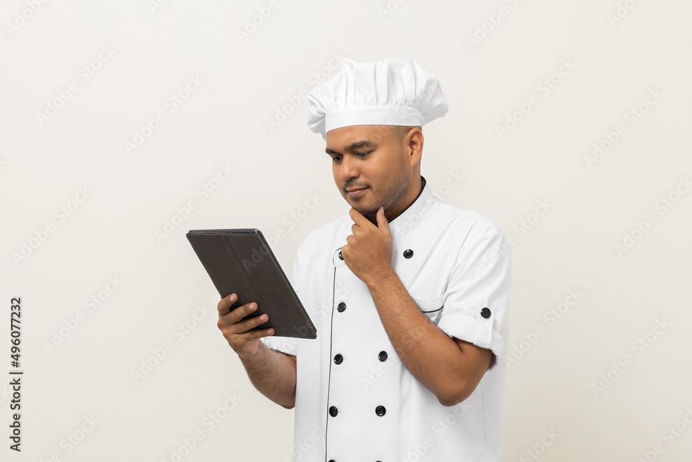 Young asian male chef holding digital tablet thinking to choose various delicious dish menu good taste for customer order. Online delivery food buying variety of dish Young asian male chef holding digital tablet thinking to choose various delicious dish menu good taste for customer order. Online delivery food buying variety of dish