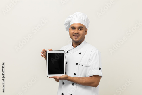 Young asian male chef holding digital tablet thinking to choose various delicious dish menu good taste for customer order. Online delivery food buying variety of dish photo