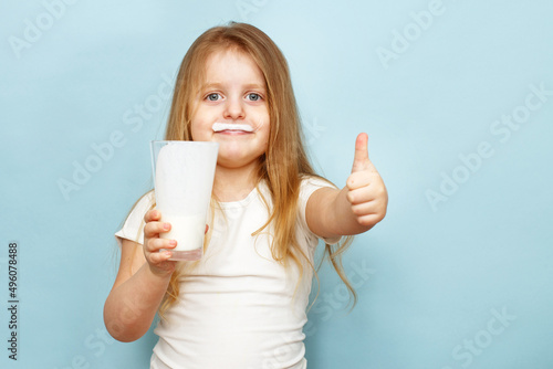 little beautiful girl holding milk in glass on a blue background. child drinks yogurt