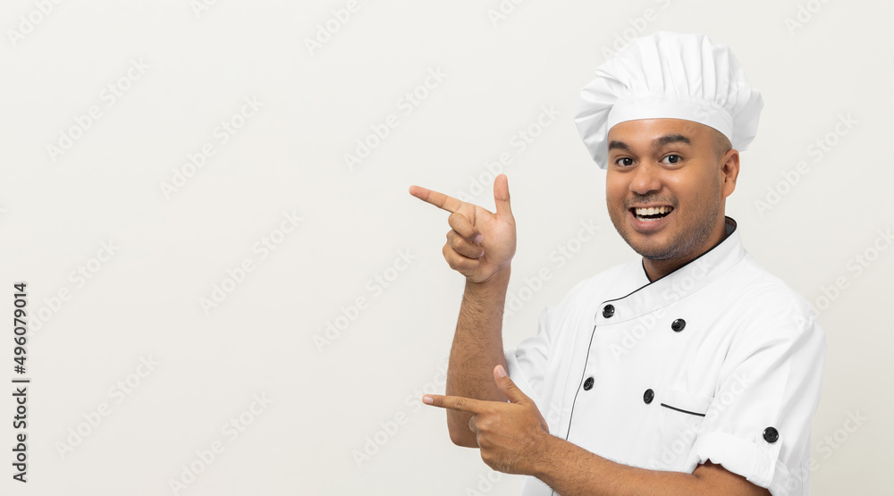 Smiling Young handsome asian man chef in uniform with hat standing pointing finger on isolated blank space for text. Cooking man Occupation chef or baker People in kitchen restaurant and hotel. Smiling Young handsome asian man chef in uniform with hat standing pointing finger on isolated blank space for text. Cooking man Occupation chef or baker People in kitchen restaurant and hotel.