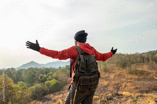 Asian young man conquers the peak success in life goals. Young asian man mountaineering wearing jacket walking at outdoor. Hiker with backpack and trekking pole.
