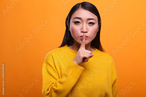 Quadro su tela Calm attractive women wearing yellow sweater making hush gesture with forefinger on orange background