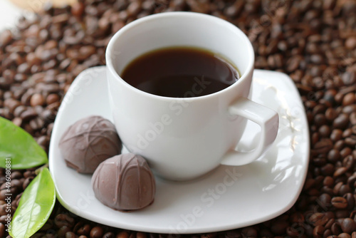 White cup of coffee with chocolate candy close up on coffee beand background