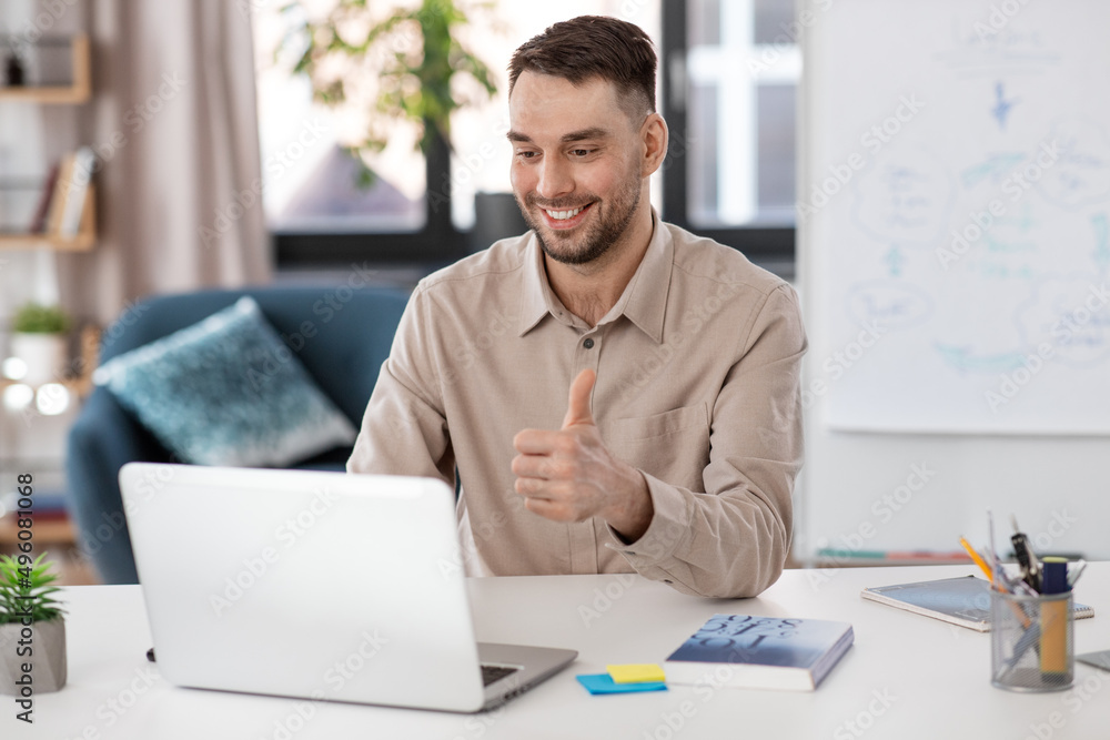 distance education, school and remote job concept - happy smiling male teacher with laptop computer having online class at home office showing thumbs up