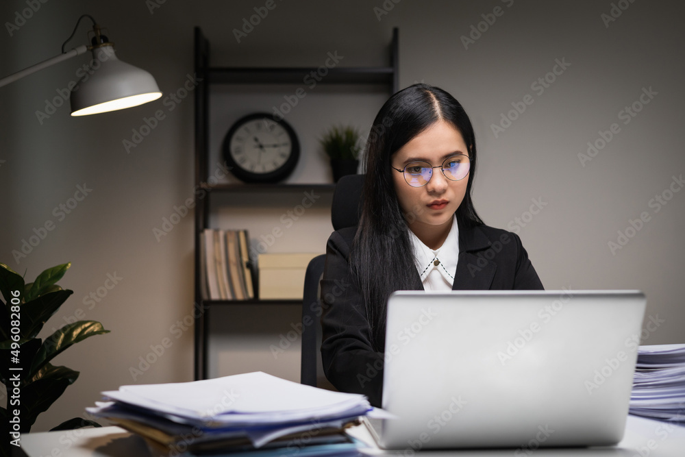 Young asian business woman working at late night. She was very busy checking paperwork and had to send the work before the deadline, feeling stressed. Sitting in the dark office at night. Young asian business woman working at late night. She was very busy checking paperwork and had to send the work before the deadline, feeling stressed. Sitting in the dark office at night.
