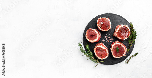 Raw beef filet Mignon steak on metel tray with pepper and salt, filet mignon. beef tenderloin steaks wrapped in bacon and thyme on light background. Long banner format. top view photo