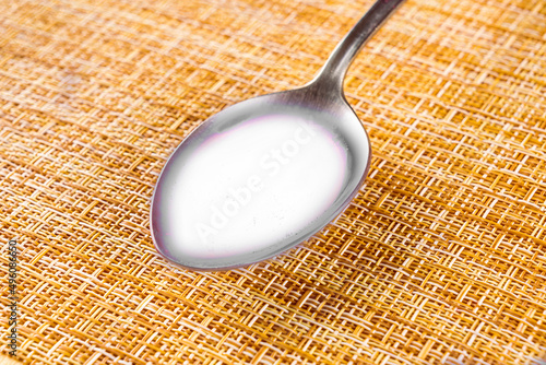 table spoon with white liquid of milk on a light brown clipped background, kitchen food and drink concept photo