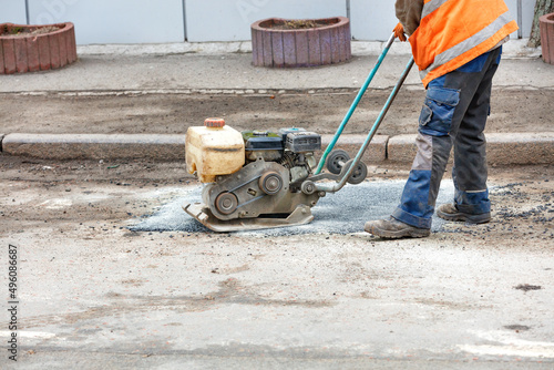 A road worker is patching up a pothole in an old road using an old petrol plate compactor.