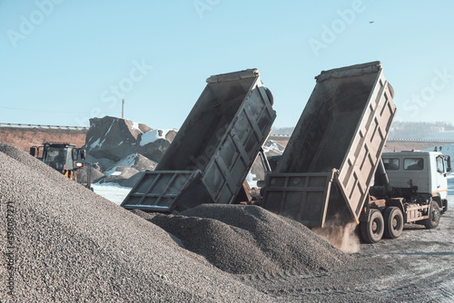 trucks carry and unload crushed stone at an asphalt concrete plant, which is needed for road construction