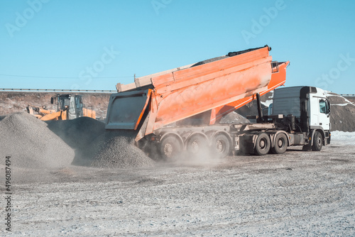 trucks carry and unload crushed stone at an asphalt concrete plant, which is needed for road construction