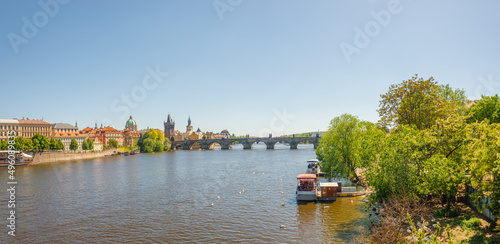 Panoramic view over magnificent Vltava river with tour boats, white swans and famous Charles Bridge and walking embarkment in historical downtown of Prague, Czech Republic at blue sunset summer sky.