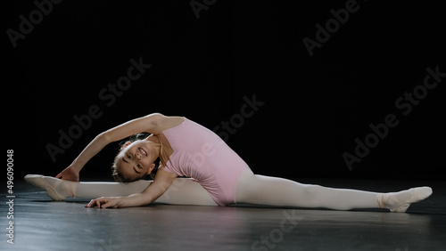 Teenager talented flexible professional acrobat ballerina dancer girl child sitting on floor on splits twine leaning to side stretching practicing acrobatic gymnastic elements training in dance class
