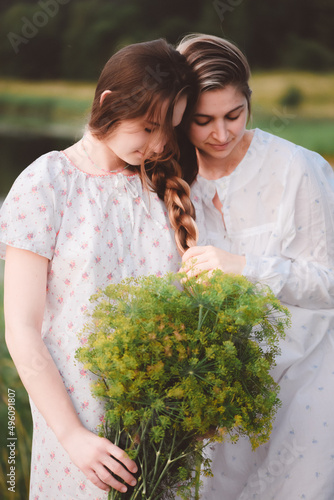 Two beautiful girls in long white nightgowns posing outdoors by the lake. The girls' hair is in one braid, sisters. Warm summer evening. Family photo, sisters. photo