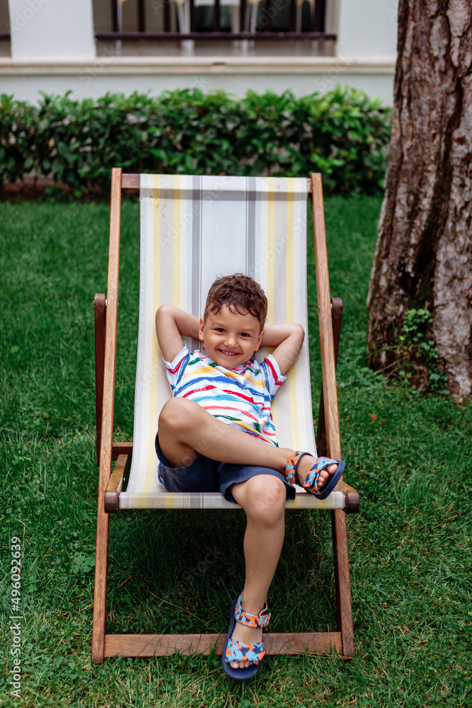 portrait of a happy boy in bright colored clothes. Summer. The boy lies on a chaise longue. 