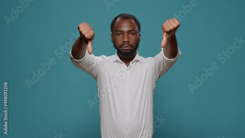 Displeased upset man showing thumbs down gesture, advertising rejection and disapproval about opinion. Unhappy negative person doing dislike symbol on camera, feeling disappointed.