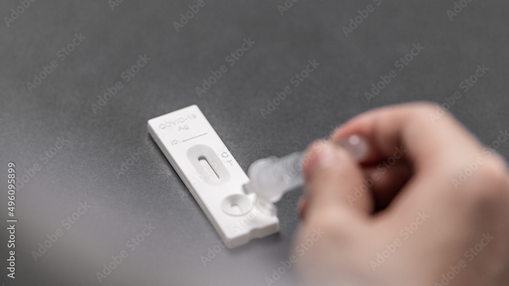 A hand dripping the extraction liquid on the cassette of a rapid antigen test A hand dripping the extraction liquid on the cassette of a rapid antigen test