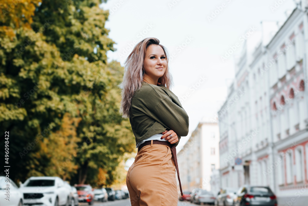Pretty hipster in youthful casual clothes with cute smile standing on street and looking away. Half-length portrait of young caucasian slim woman posing in city at daytime outdoors. Summer lifestyle Pretty hipster in youthful casual clothes with cute smile standing on street and looking away. Half-length portrait of young caucasian slim woman posing in city at daytime outdoors. Summer lifestyle