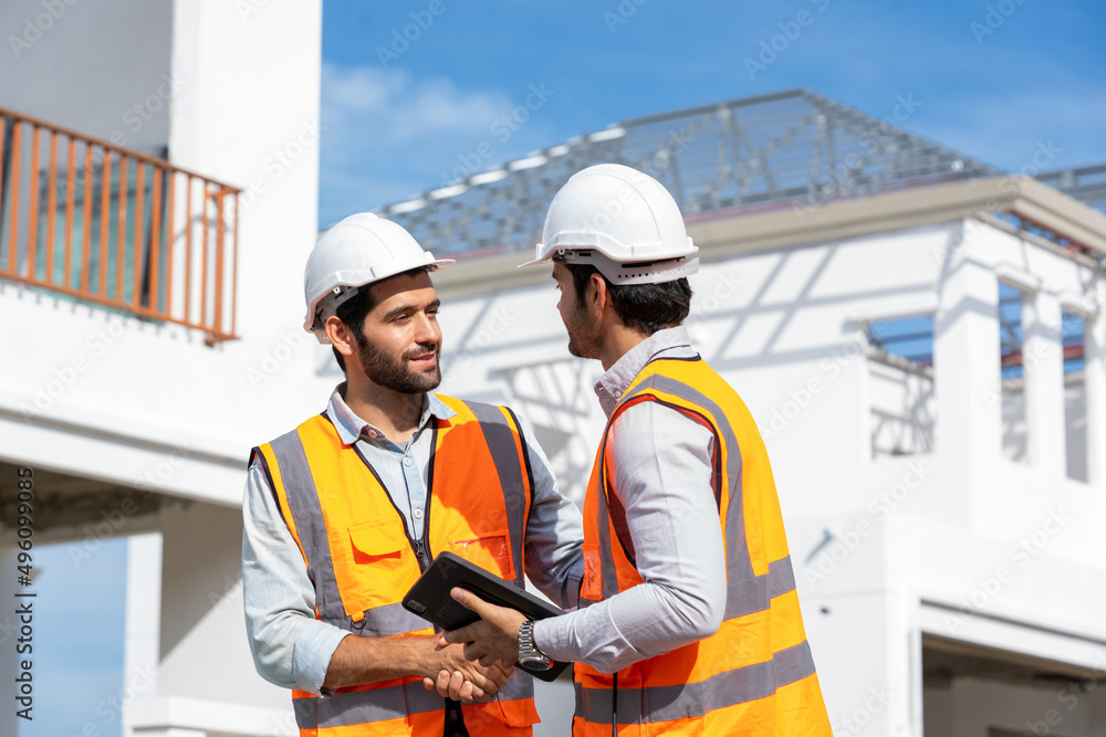Engineer and architect in protective helmets and vests are shaking hands while working in construction site. Engineer and architect in protective helmets and vests are shaking hands while working in construction site.