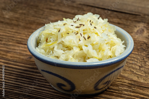 Homemade pickled sauerkraut with caraway seeds in a bowl on a wooden board
