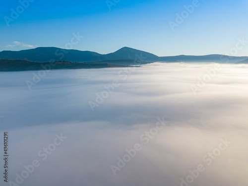 Flight over fog in Ukrainian Carpathians in summer. Mountains on the horizon. A thick layer of fog covers the mountains with a continuous carpet. Aerial drone view.