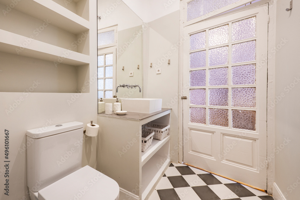 Toilet with built-in washbasin cabinet with white porcelain sink, wooden door with opaque glass and checkered tiled floors Toilet with built-in washbasin cabinet with white porcelain sink, wooden door with opaque glass and checkered tiled floors