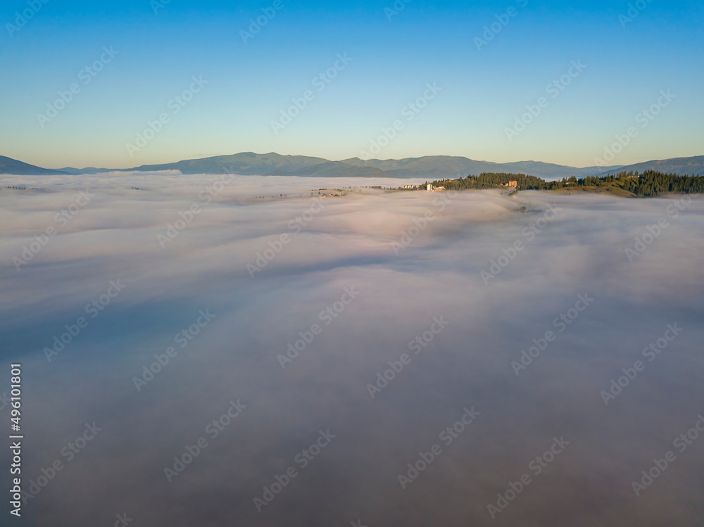 Fototapeta premium Sunny morning in the foggy Carpathians. A thick layer of fog covers the mountains. Aerial drone view.