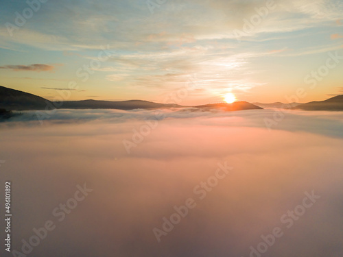 The rays of dawn over the fog in the Ukrainian Carpathians. Aerial drone view. © Sergey