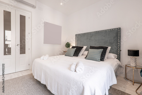 Wallpaper Mural Bedroom with studded blue velvet headboard, lots of cushions on the bed and white woodwork Torontodigital.ca