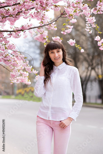 Young beautiful girl standing near the sakura blossom on the city street