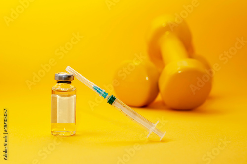 syringe and a jar of liquid stand next to dumbbells on a yellow background, a horizontal picture. the concept of doping in sports, steroids, testosterone and other drugs banned in sports.