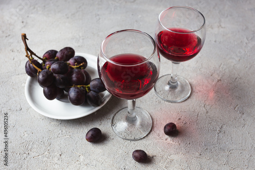 two glasses with red wine and grapes on a concrete background