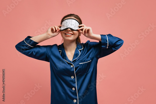 Half-length portrait of young beautiful woman in silk pajamas wearing sleeping mask, posing isoated over pink studio background photo