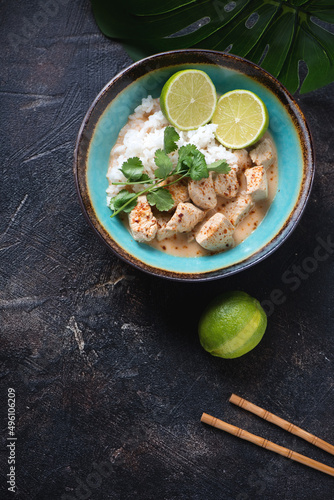 Turquoise bowl of thai red curry with chicken, coconut milk and rice, flat lay on a dark-brown stone background, vertical shot with copyspace