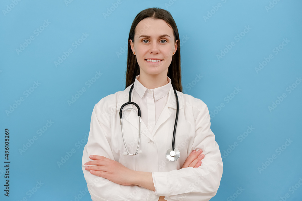 Confident smiling female doctor wear white medical coat, stethoscope look at camera standing on blue color background wall. Happy young woman health care professional medical practitioner physician Confident smiling female doctor wear white medical coat, stethoscope look at camera standing on blue color background wall. Happy young woman health care professional medical practitioner physician