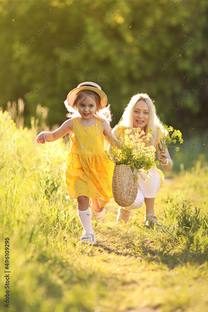 Fototapeta premium Mother and little daughter having fun in summer meadow with yellow flowers. Happy family on summer. Concept of healthy family without allergies. High quality photo