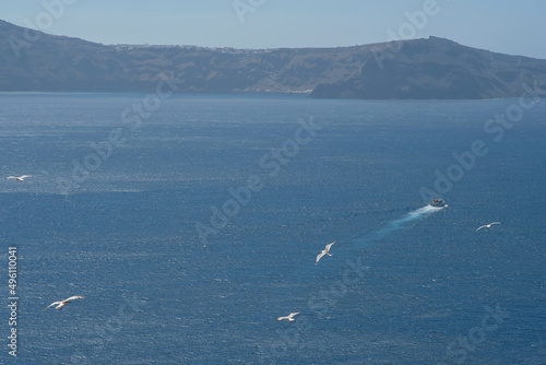 View of a small ferry boat that just left the harbour of Santorini and seagulls flying above it photo