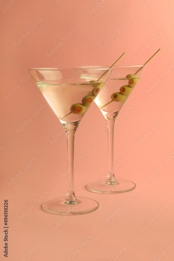 two martini glasses with olives on pink background