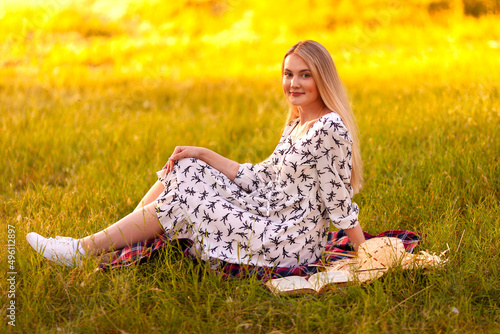 blonde woman in a light dress resting on the grass in summer