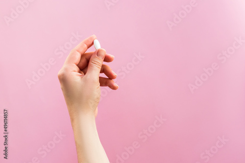 Woman holding one white pill on pink background.