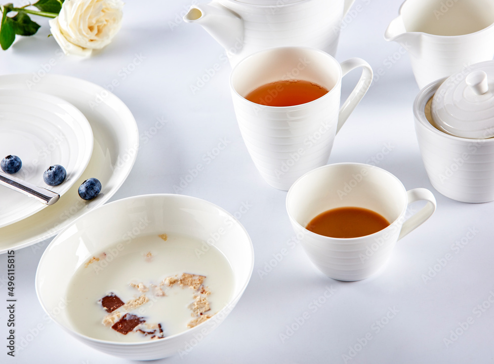 Breakfast milk cereal and tea with blueberries in white cutlery Breakfast milk cereal and tea with blueberries in white cutlery