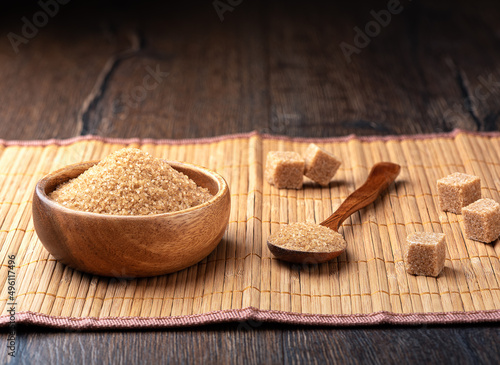Wooden bowl and spoon with cane sugar, sugar cubes on a food mat.