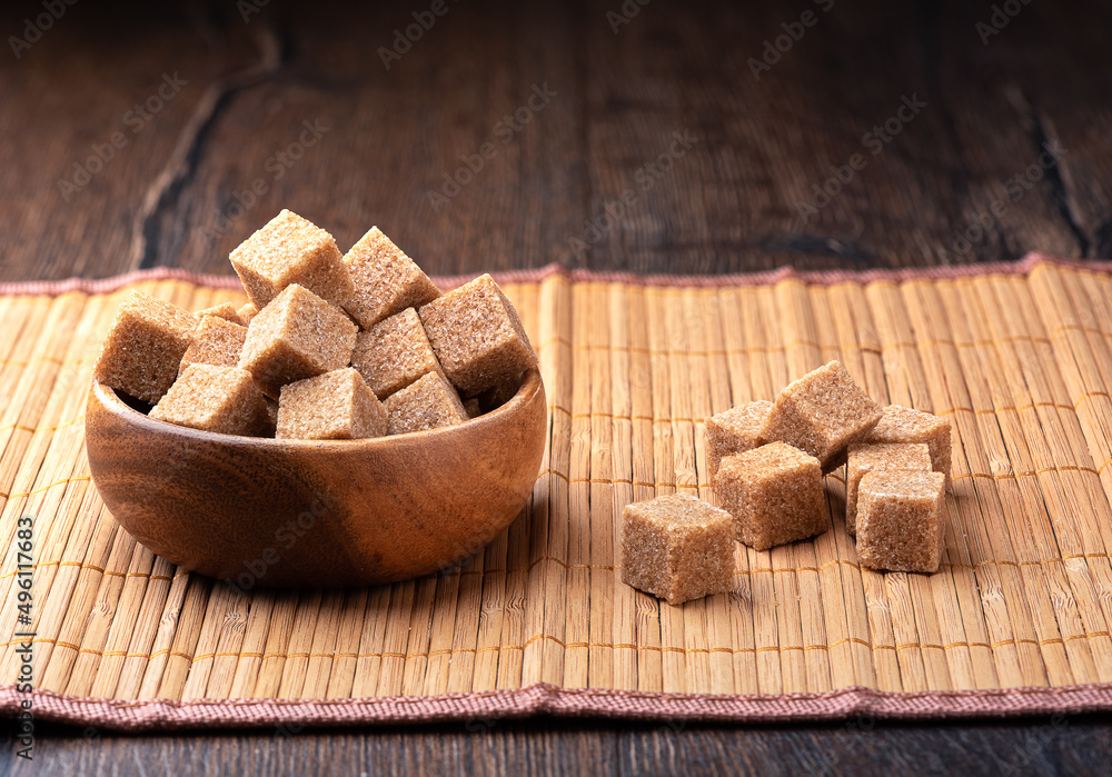 A wooden bowl full of cane sugar cubes and individual cubes on a food mat. A wooden bowl full of cane sugar cubes and individual cubes on a food mat.