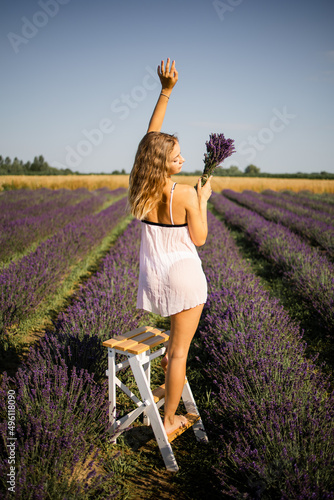Fototapeta Naklejka Na Ścianę i Meble -  Back view of unrecognizable blonde in summer white dress walking on lavender fields 
