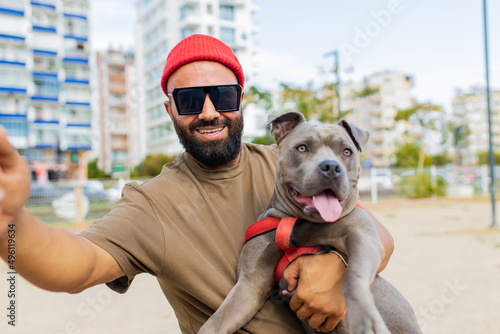 portrait of happy man in red hat and sunglasses with american terrier in dogs walking area park in sity