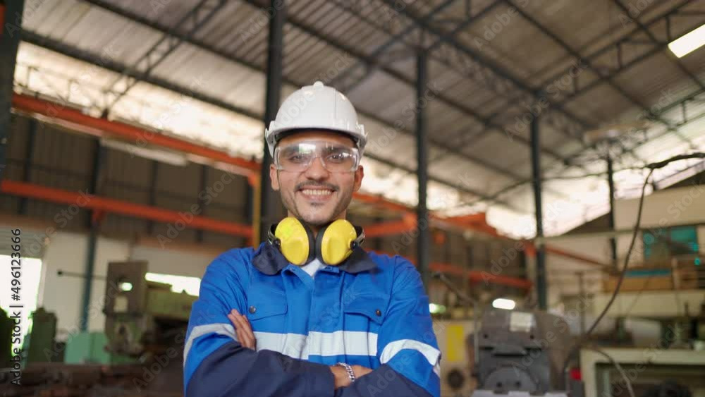 Close up portrait of confident engineer man wearing safety helmet and glasses standing in the CNC manufacturing factory. Looking forward and crossed arm. Technology and industrial concept Close up portrait of confident engineer man wearing safety helmet and glasses standing in the CNC manufacturing factory. Looking forward and crossed arm. Technology and industrial concept